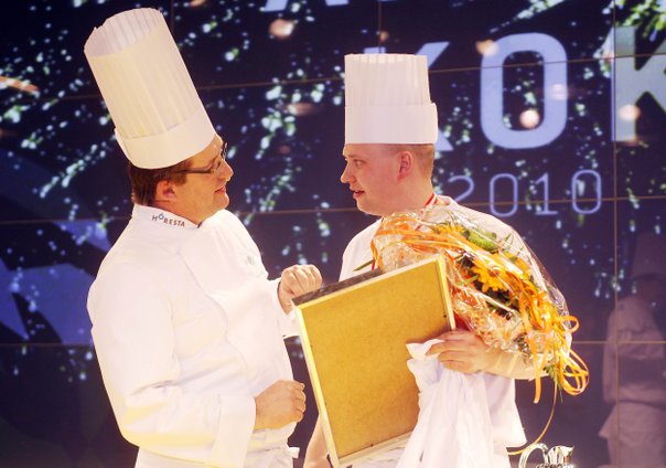 Dommer Per Mandrup med hvid kokkehue og hvid kokkejakke overrækker blomster og diplom til kok, Tommy Friis, med hvid kokkehue og kokkejakke til Årets Kok 2010