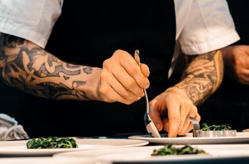 Kok med tatoveringer anrettet spinat på en hvid tallerken